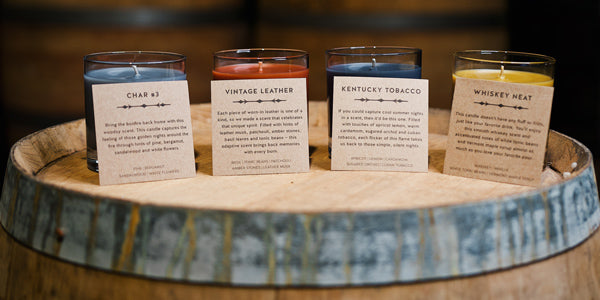 Char 3, vintage leather, Kentucky tobacco and whiskey neat candles with description cards set on top of a barrel