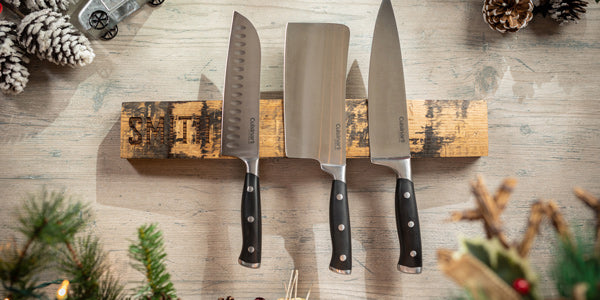 Three large knifes on whiskey barrel stave with last name Smith engraved on one end and pine tree branches and pine cones nearby