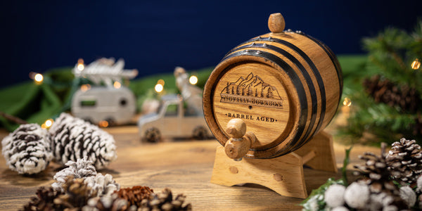 An engraved small liter oak barrel with mountains engraved on the head and pinecones and evergreen decor around the barrel