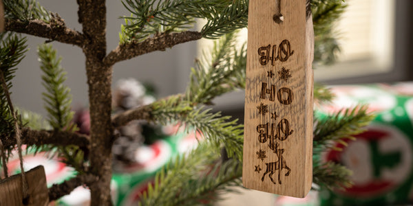 Wine barrel ornament hanging on a Christmas tree with engraved text Ho Ho Ho and drawing of a reindeer 