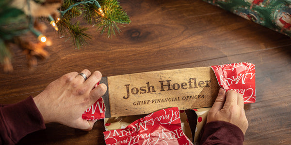 Person unwrapping a desk plate theme engraved whiskey barrel stave gifted as a present under the tree