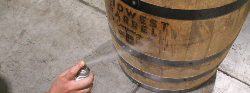 Person spraying protective coating on barrel with engraving Midwest Barrel Company logo on the side.