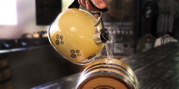 Filling oak aging barrel with hot water from a kettle to swell