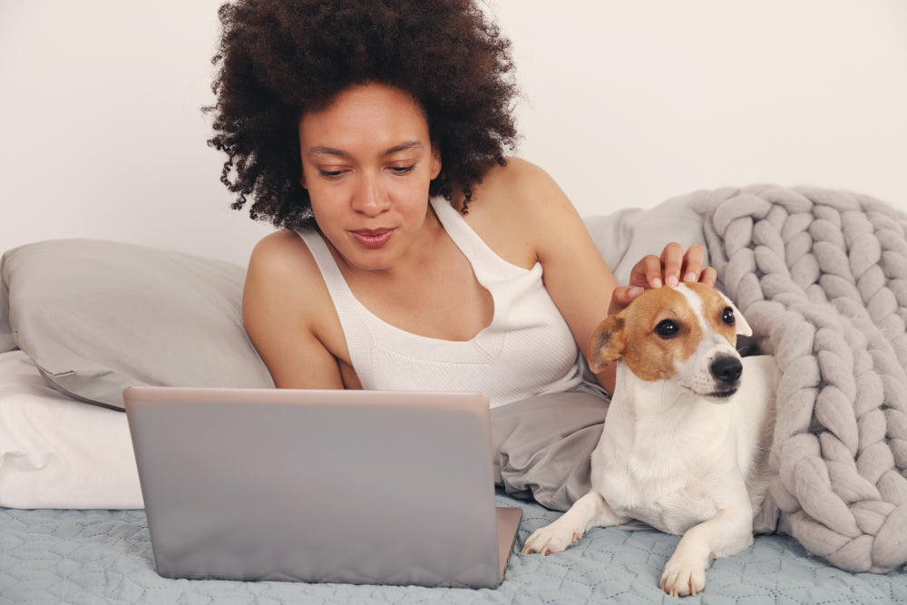 Young Black woman petting dog while laying in bed waiting for an online vet appointment
