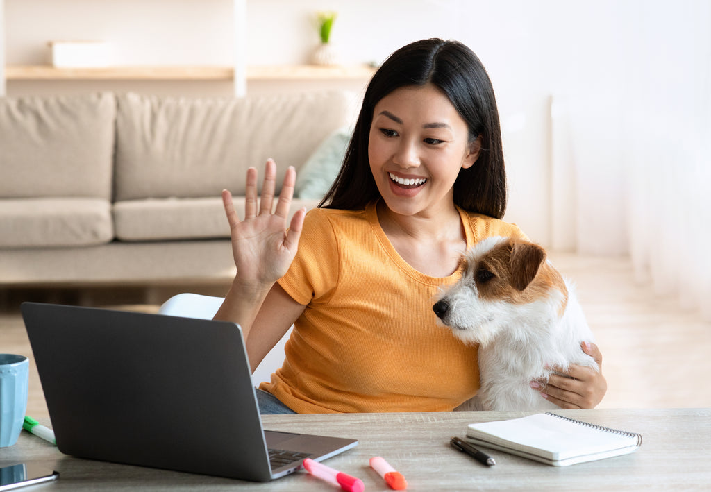 Woman waving during a video call on her laptop with hand around dog