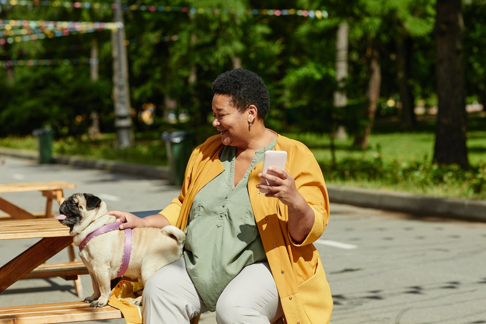 Middle aged Black woman smiling at her pug while sitting at a picnic table