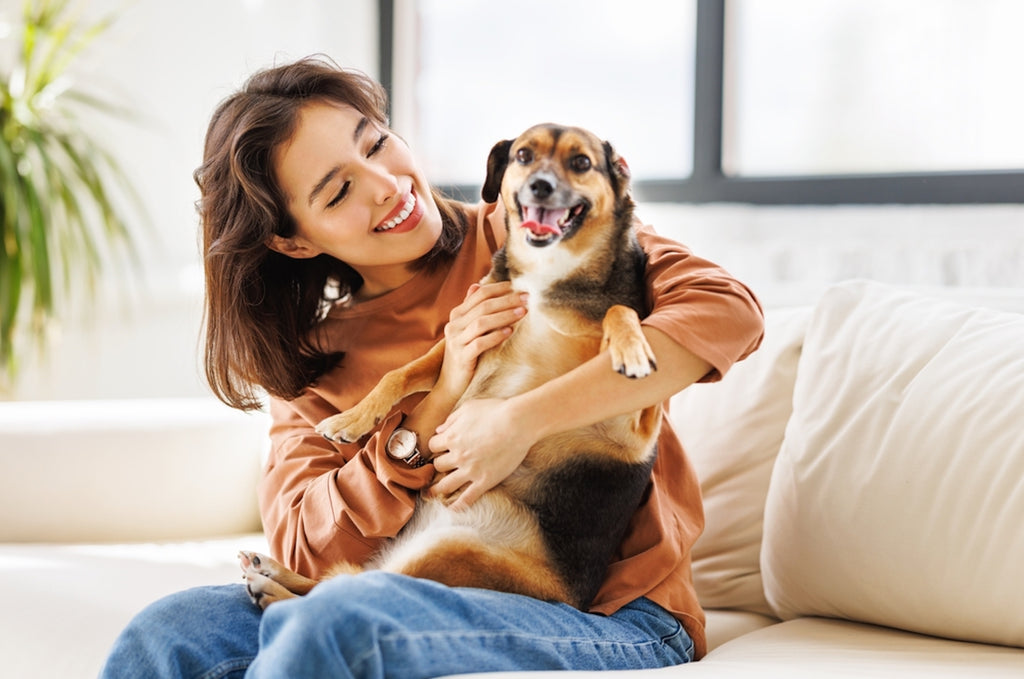 Happy young woman holding her dog while sitting on the couch