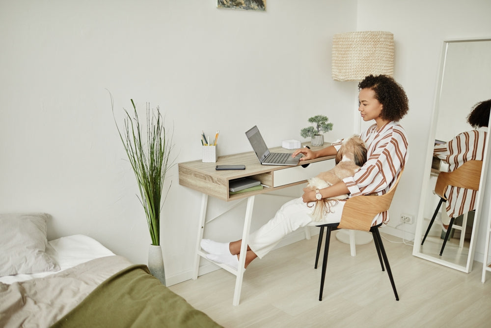 Black woman sitting at desk with dog in lap, waiting for an online vet consultation