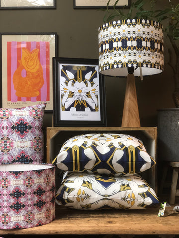 bright and abstract design cushions and lampshade by Rhoma Design stacked on a wooden table