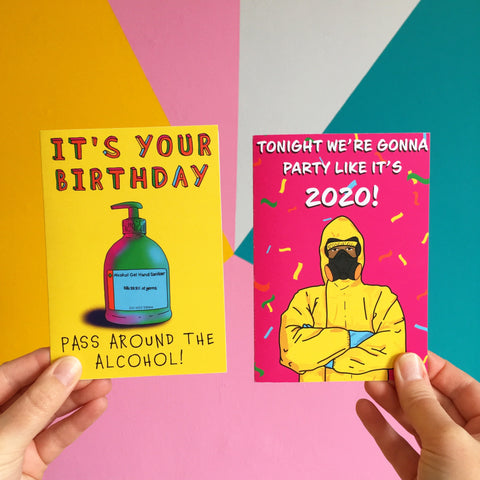 A hand holds two brightly coloured cards. One has an illustration of hand sanitizer and the words 'it's your birthday, pass around the alcohol' and the other has an illustration of a person in a HAZMAT suit and the words 'tonight we're gonna party like its 2020'