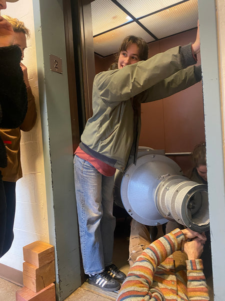 a pug mill is placed into an elevator with a person holding the door open
