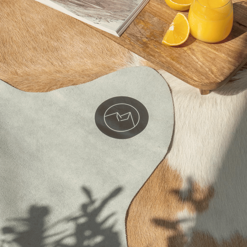 Animated image (GIF) showing a close-up of a hand revealing the back of a Palomino and White Cowhide Rug, highlighting its natural underside and brand logo.