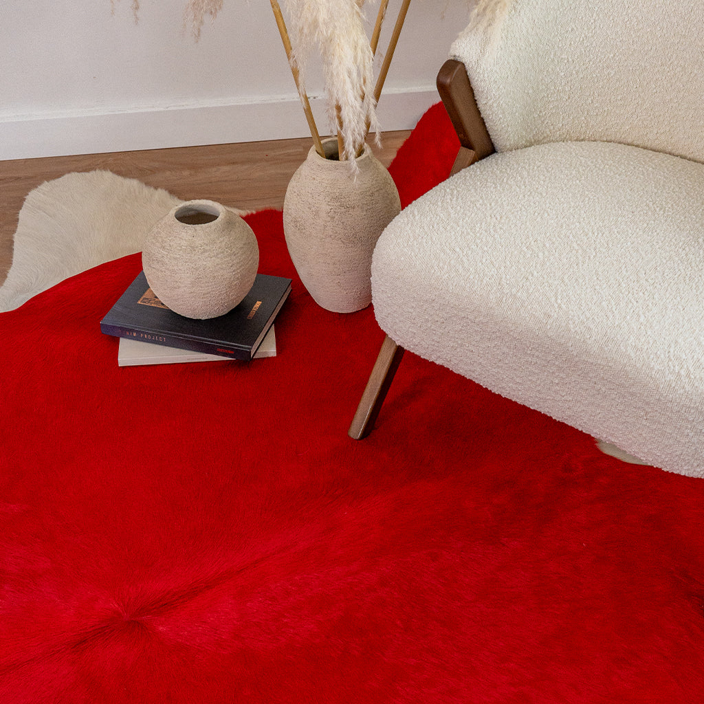 Red Cowhide Rug on a light wood floor in a cozy room with a white armchair and decor.