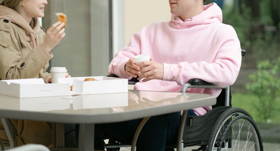 ragazzo su sedia a rotelle ad un tavolo con una ragazza come metafora della possibilità di coltivare la sessualità nella disabilità