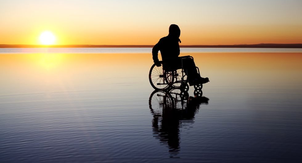 ragazzo su sedia a rotelle sulla spiaggia al tramonto