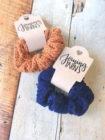 Two scrunchies, one copper and one navy, against a wooden background.