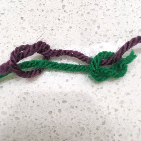 A purple strand of yarn being joined with a green strand of yarn