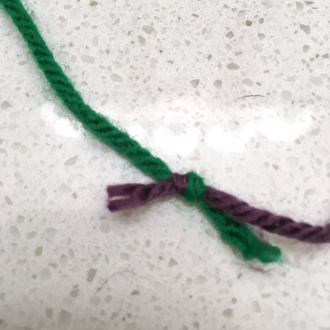 A green strand of yarn joined with a purple strand of yarn