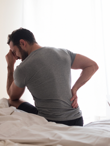 Man sitting on bed in pain doesn't know how to sleep with piriformis syndrome