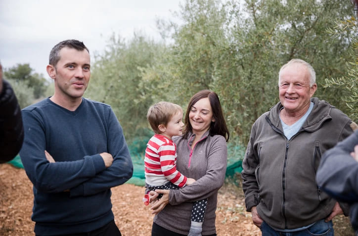 Famille souriante avec une femme tenant un enfant dans les bras devant des oliviers