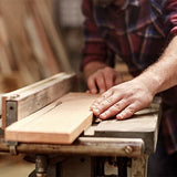hands holding plan of wood in place on top of saw