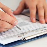 hand holding pen writing on paper attached to clipboard