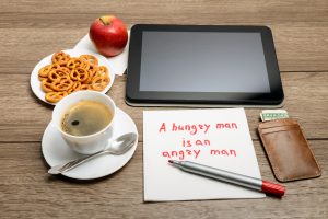 napkin handwriting message proverb on wooden table with coffee, some food and tablet PC A hungry man is an angry man