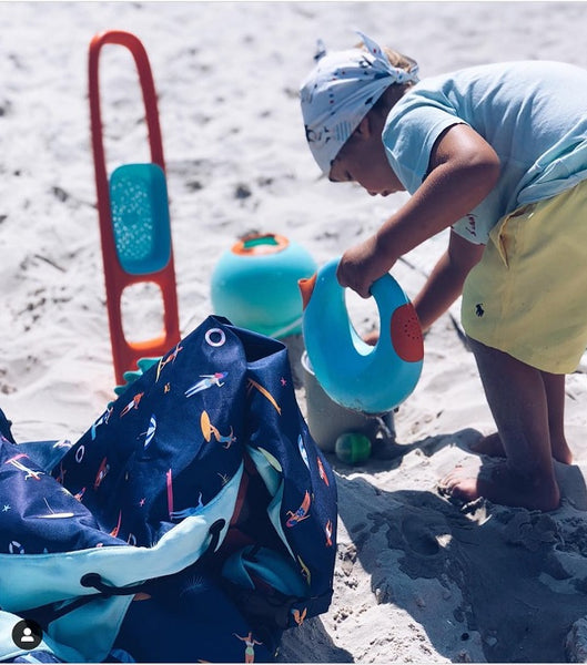 Garçon jouant avec un arrosoir sur la plage avec des jouets de plage autour