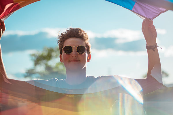 Closeup shot of young individual outside, holding up pride flag in the wind.