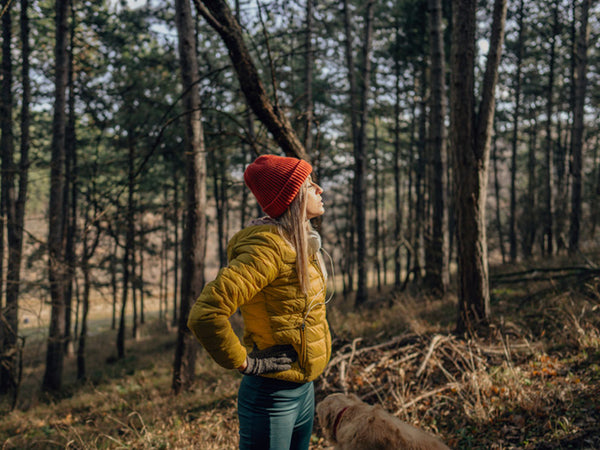 Woman standing in woods with hands on hips, eyes closed with face directed towards the sun.