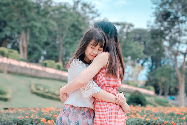 Two young girls outside embracing each other in a loving way.