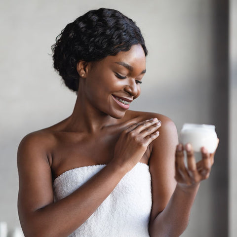 smiling woman applying body butter to her shoulder