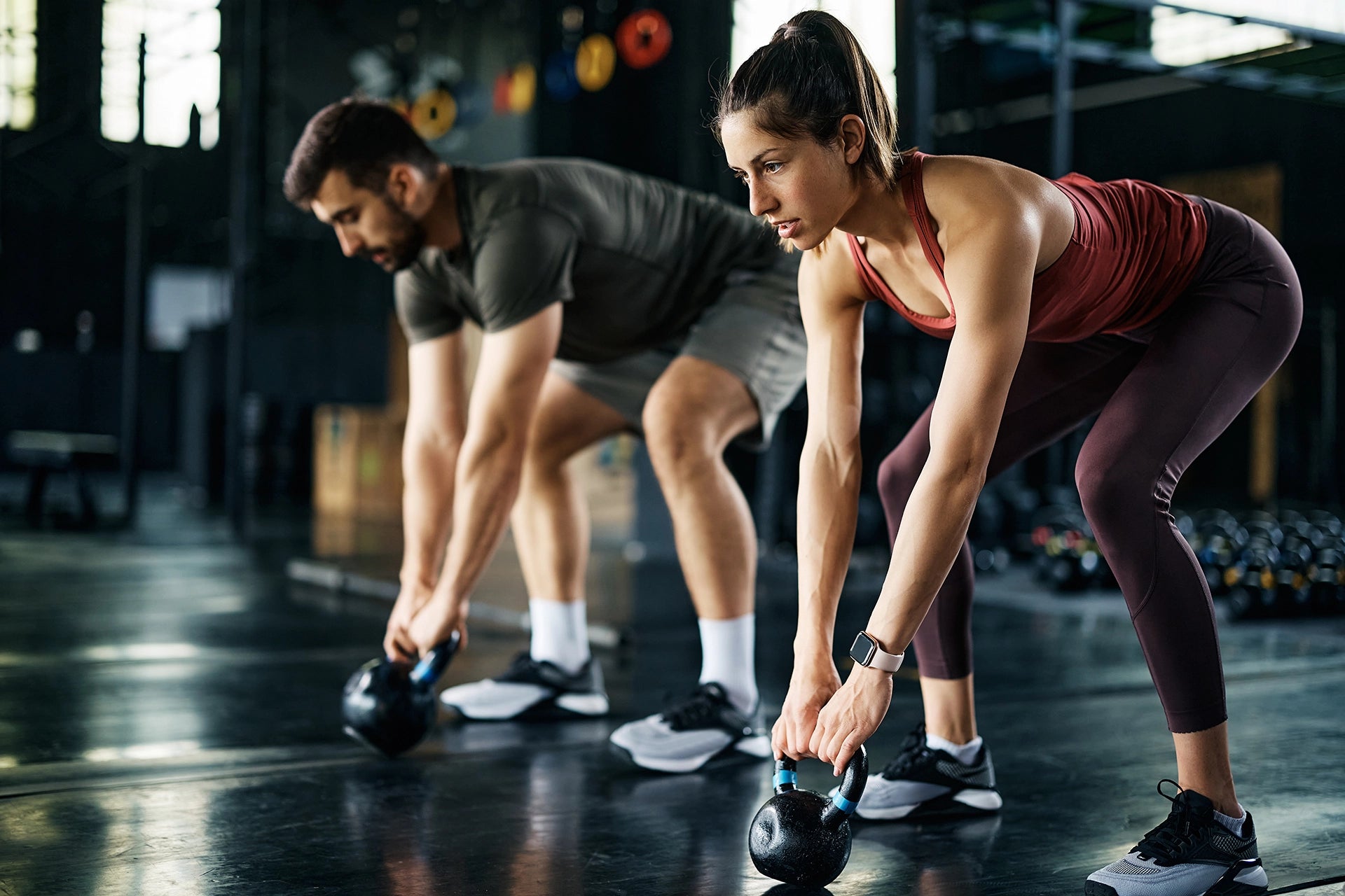 Young athletic couple exercising with kettle bells during cross training at gym.