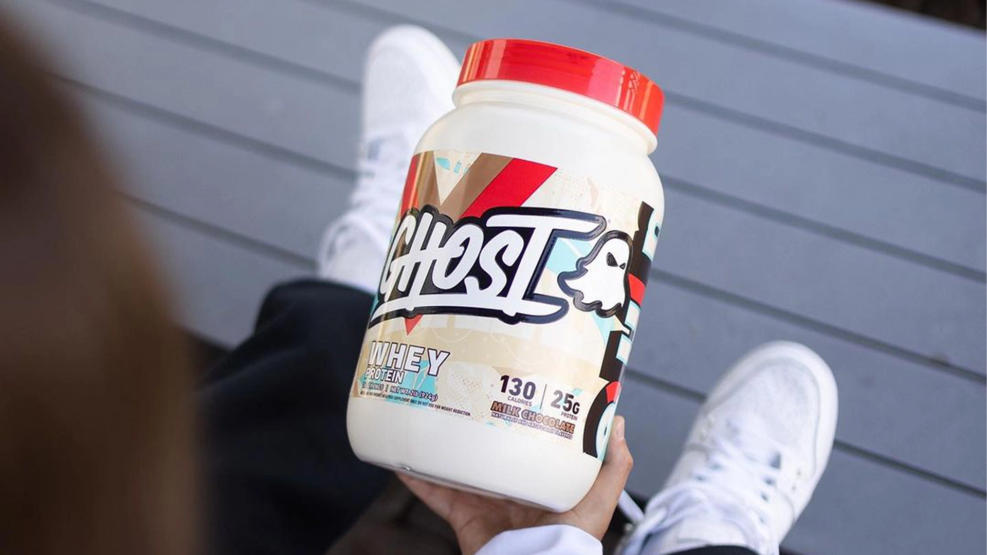 Person holding a tub of Ghost Whey