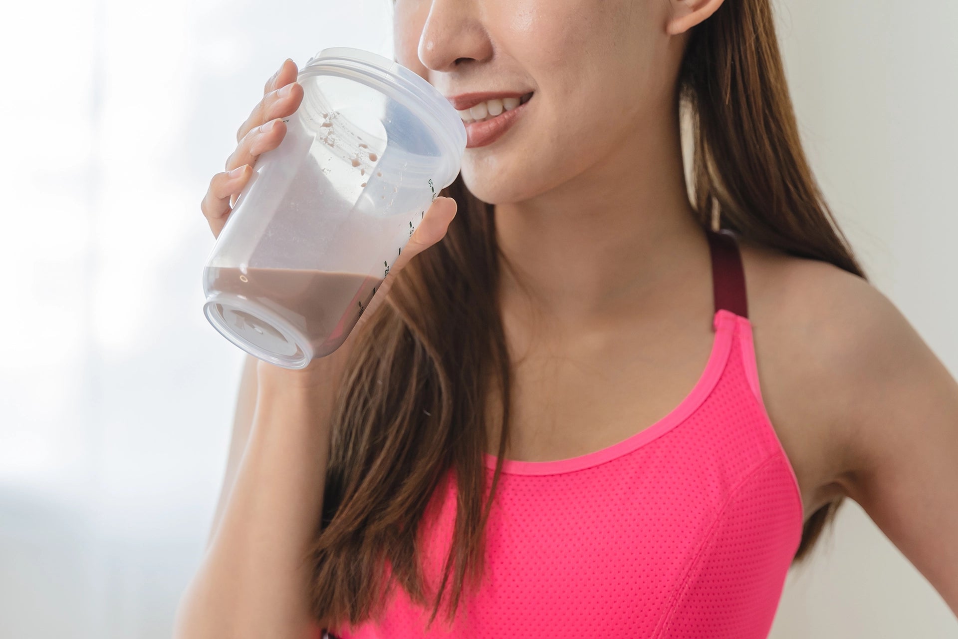 Young woman drinking protein powder from a shaker cup