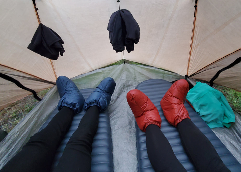 sleep accouterments: down booties on legs laying on two sleeping pads in a tent