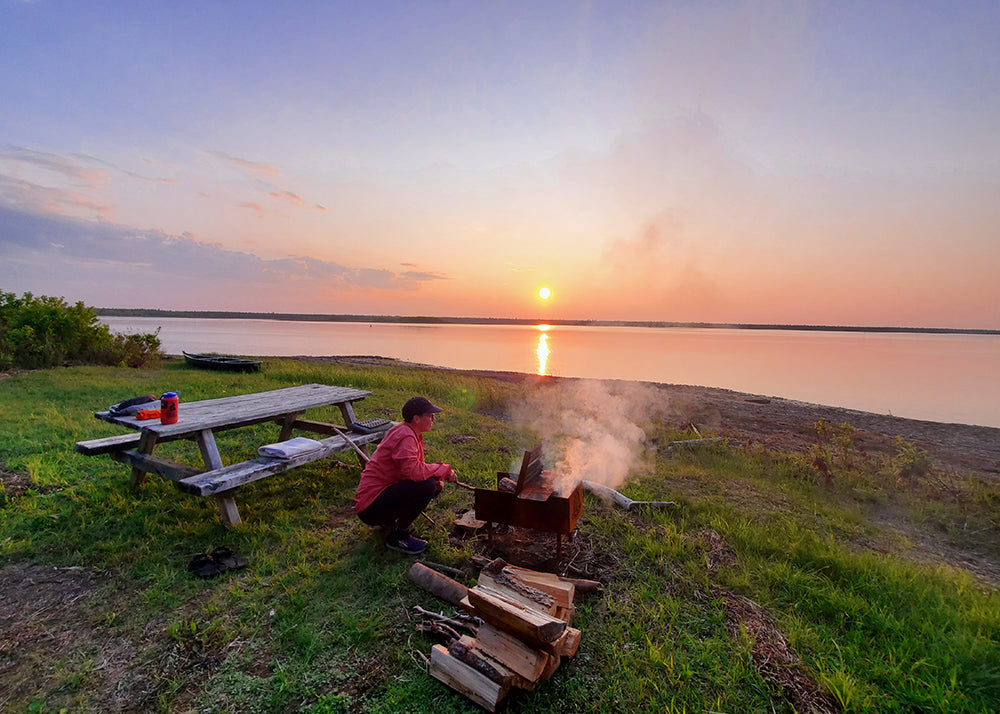 sunset over a lake with a person making a fire