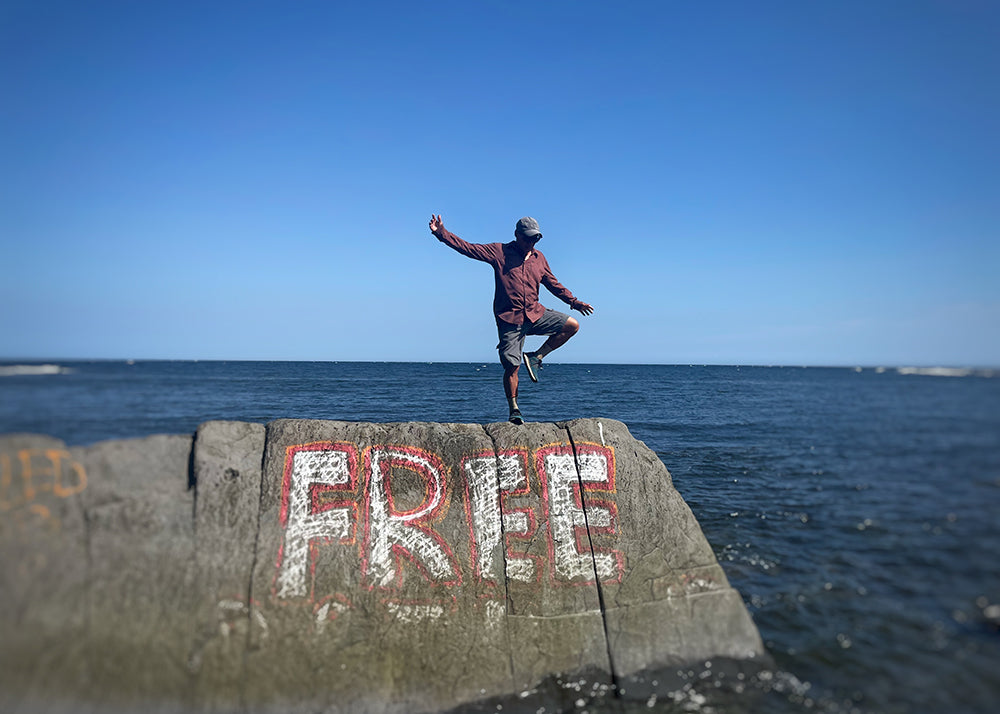 lil buddha standing on a wall in the ocean that says "free" painted on it