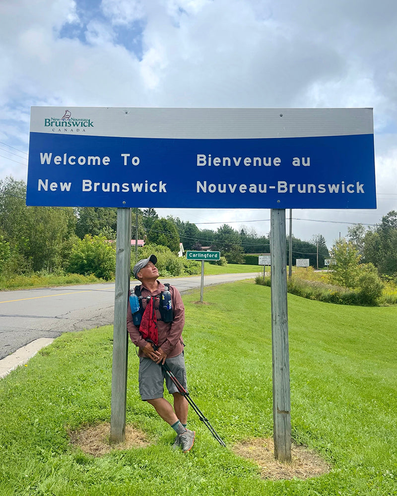 lil buddha stands under a New Brunswick sign in Canada