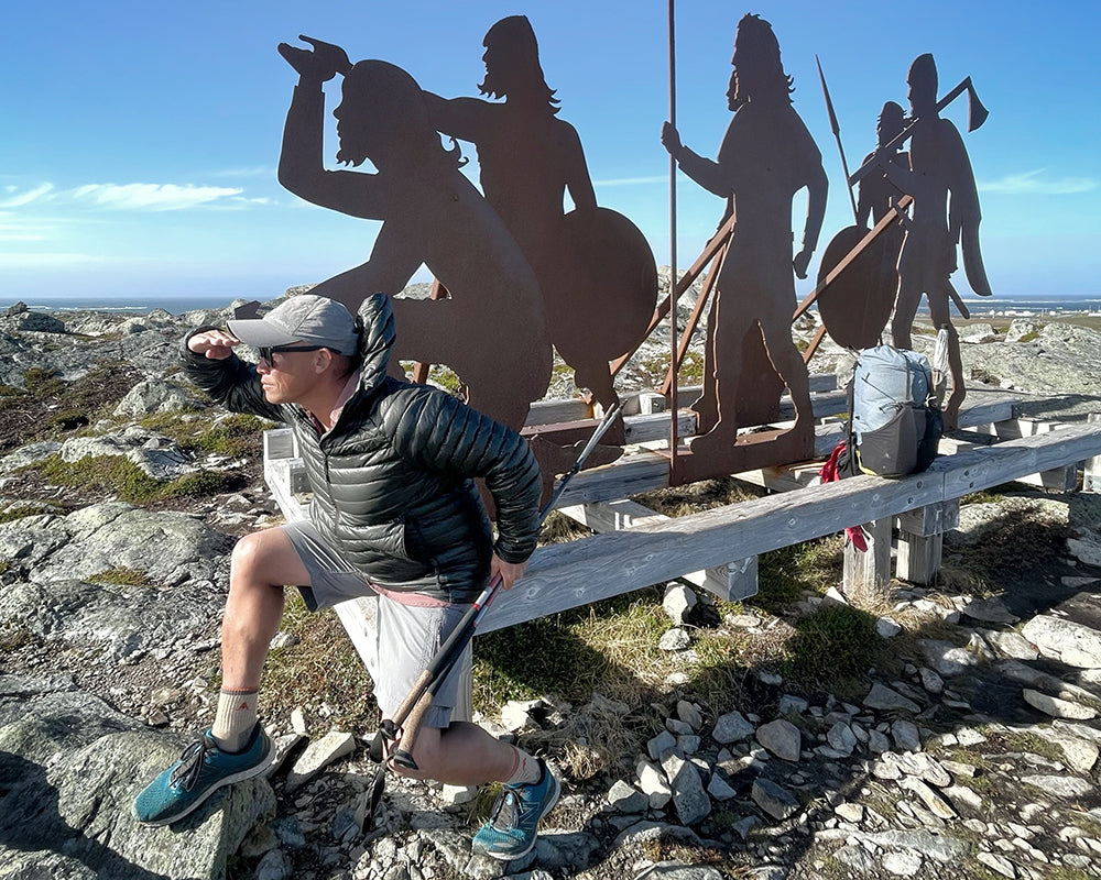 hiker lil buddha stands looking into the distance with iron work behind him