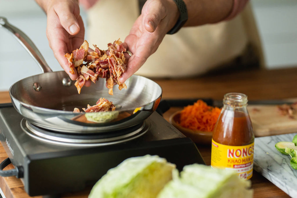 Chef adding bacon to the skillet.