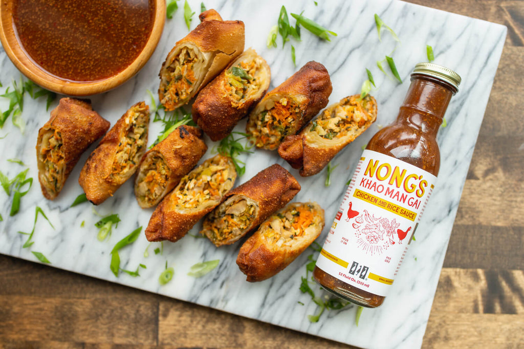 Finished egg rolls pictured with Nong's sauce on a marble serving tray.