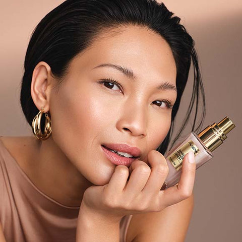 Model with gold earrings holding Anew Renewal Power Serum bottle.