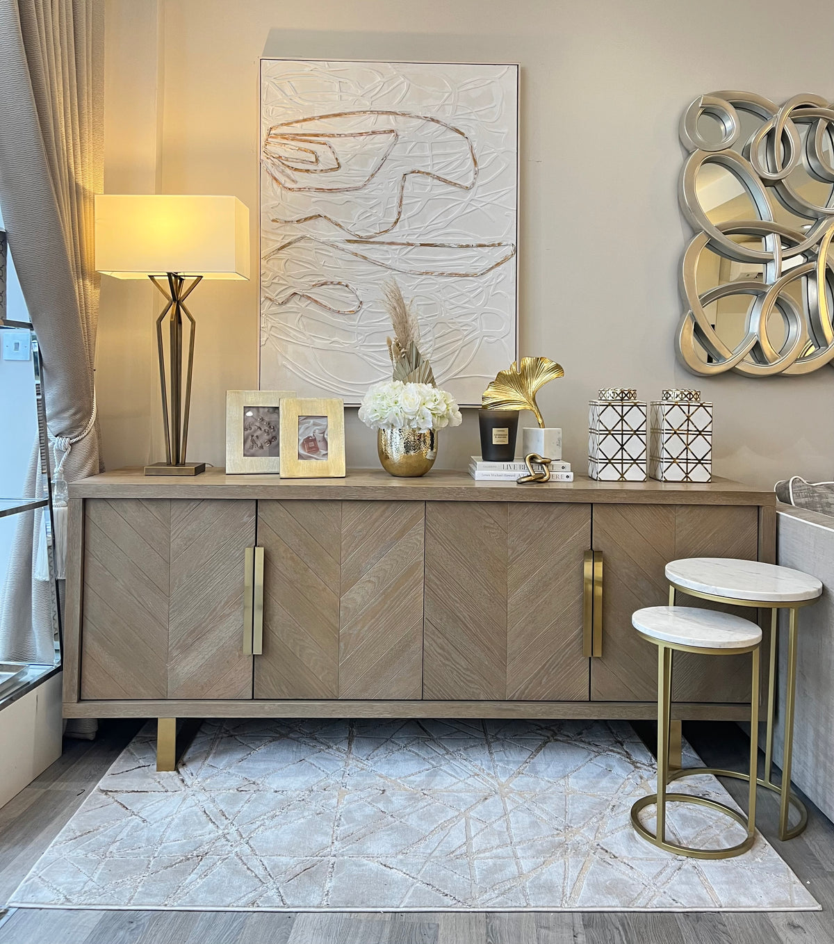 gold home interiors. Wooden herringbone sideboard with gold accessories, brass lamp and artificial flowers
