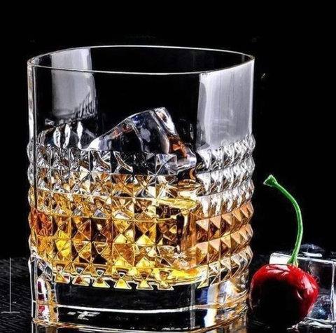 Whisky tumbler next to an ice cube and red cherry.