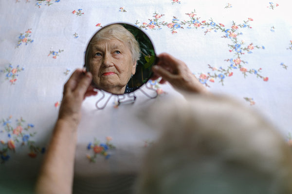 pensive elderly woman reflecting a small round mirror she is holding