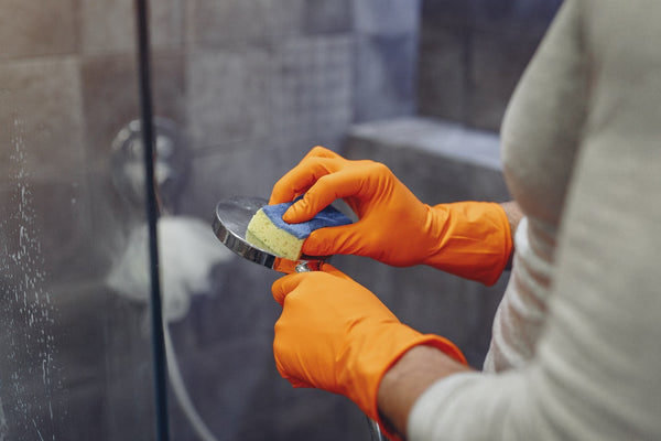 person wearing orange gloves cleaning back of shower head