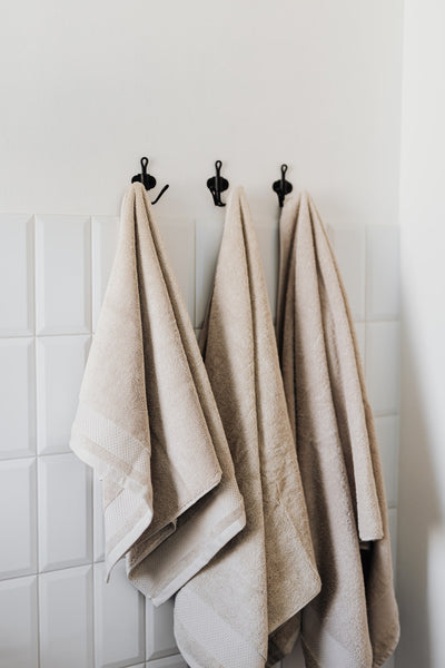 three beige towels hanging from three black towel hooks on the bathroom wall