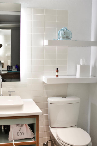 white bathroom with floating shelves and ledges on top of toilet tank 