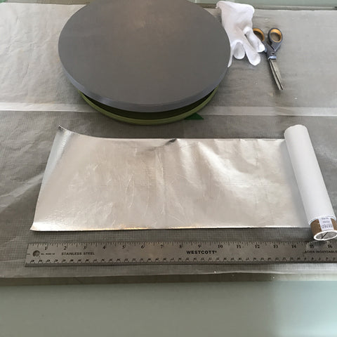 Roll of metal leaf with wooden circular panel, cotton gloves and scissors on a table